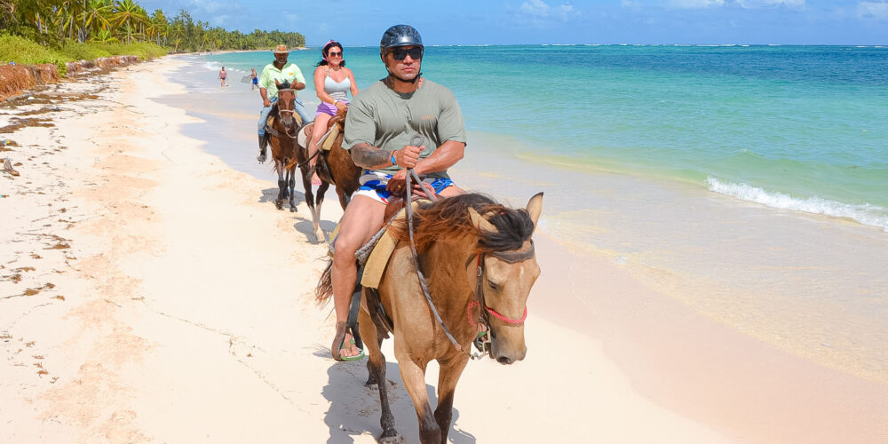 Scenic horse riding experience on the beach, with riders trotting along the shoreline, the gentle waves lapping at their feet, and the sun setting in the background, creating a tranquil and picturesque coastal adventure.