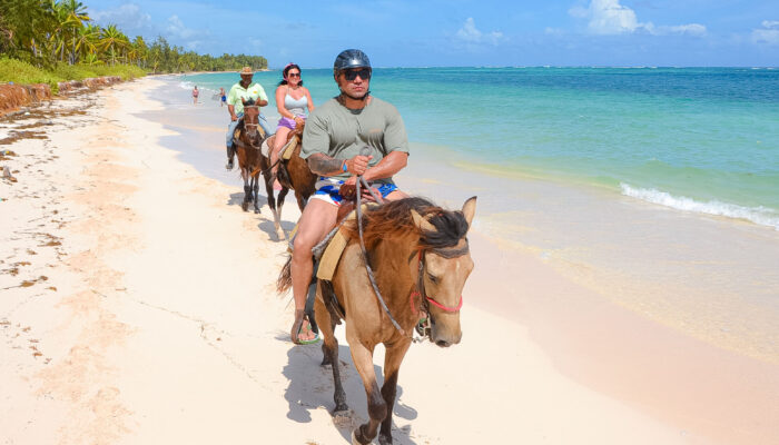 Scenic horse riding experience on the beach, with riders trotting along the shoreline, the gentle waves lapping at their feet, and the sun setting in the background, creating a tranquil and picturesque coastal adventure.