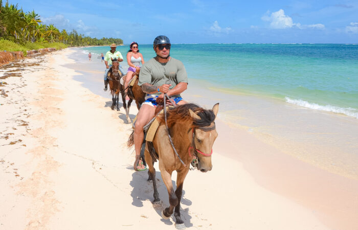 Scenic horse riding experience on the beach, with riders trotting along the shoreline, the gentle waves lapping at their feet, and the sun setting in the background, creating a tranquil and picturesque coastal adventure.