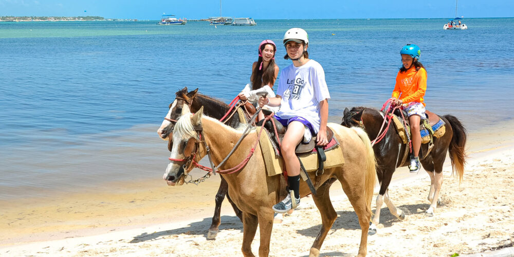 Scenic horse riding experience on the beach, with riders trotting along the shoreline, the gentle waves lapping at their feet, and the sun setting in the background, creating a tranquil and picturesque coastal adventure.