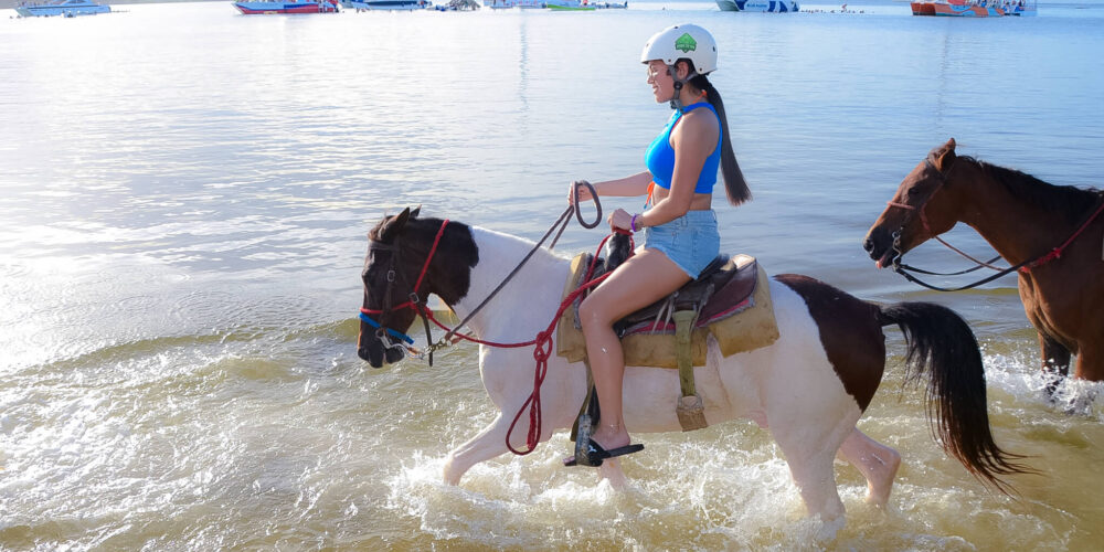 Scenic horse riding experience on the beach, with riders trotting along the shoreline, the gentle waves lapping at their feet, and the sun setting in the background, creating a tranquil and picturesque coastal adventure.