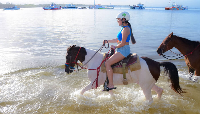 Scenic horse riding experience on the beach, with riders trotting along the shoreline, the gentle waves lapping at their feet, and the sun setting in the background, creating a tranquil and picturesque coastal adventure.