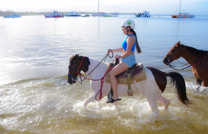 Scenic horse riding experience on the beach, with riders trotting along the shoreline, the gentle waves lapping at their feet, and the sun setting in the background, creating a tranquil and picturesque coastal adventure.