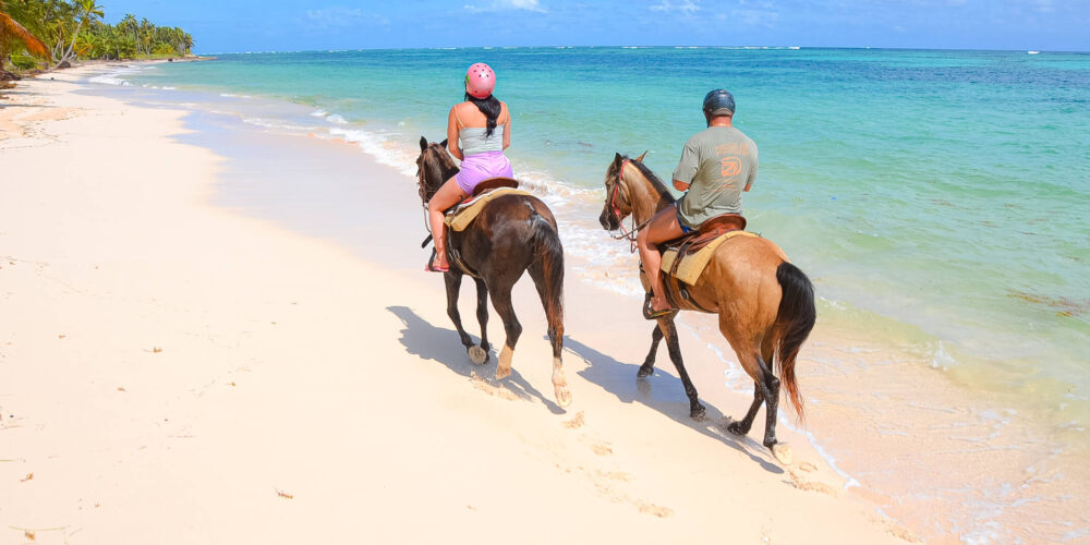 Scenic horse riding experience on the beach, with riders trotting along the shoreline, the gentle waves lapping at their feet, and the sun setting in the background, creating a tranquil and picturesque coastal adventure.