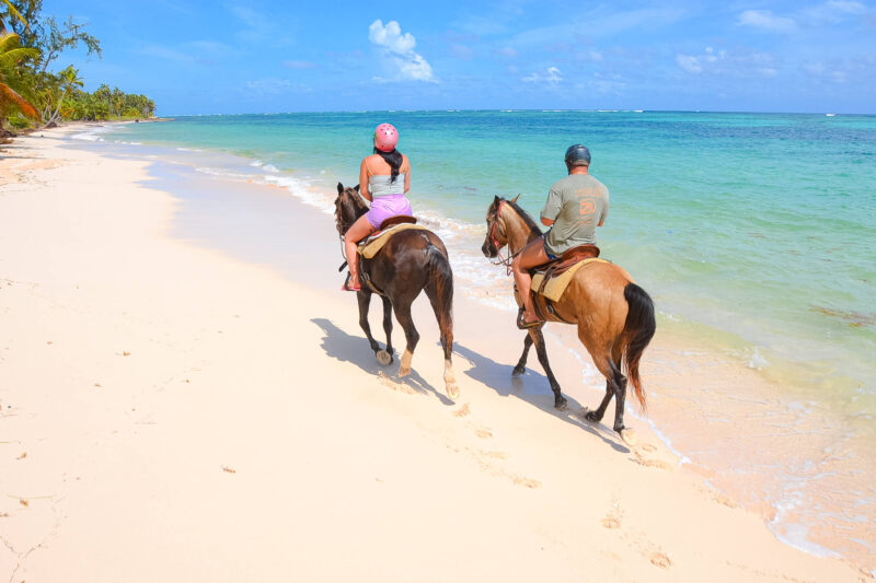 Scenic horse riding experience on the beach, with riders trotting along the shoreline, the gentle waves lapping at their feet, and the sun setting in the background, creating a tranquil and picturesque coastal adventure.