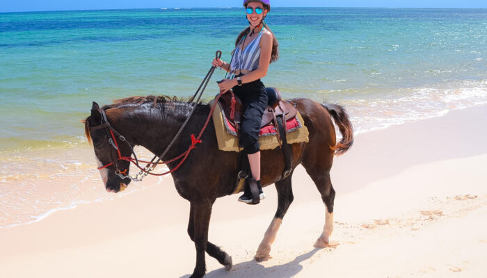 Scenic horse riding experience on the beach, with riders trotting along the shoreline, the gentle waves lapping at their feet, and the sun setting in the background, creating a tranquil and picturesque coastal adventure.