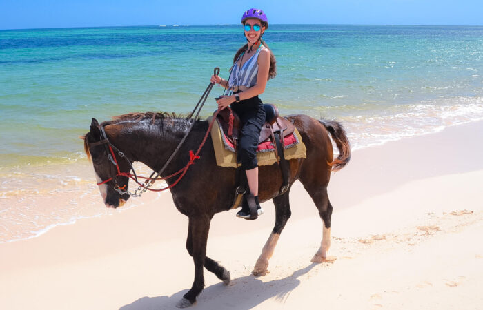 Scenic horse riding experience on the beach, with riders trotting along the shoreline, the gentle waves lapping at their feet, and the sun setting in the background, creating a tranquil and picturesque coastal adventure.