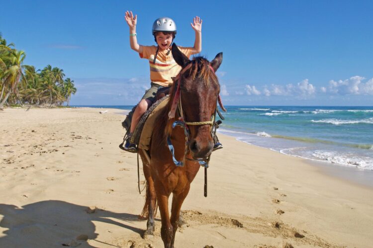 Scenic horse riding experience on the beach, with riders trotting along the shoreline, the gentle waves lapping at their feet, and the sun setting in the background, creating a tranquil and picturesque coastal adventure.