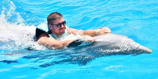 Memorable dolphin swim experience, with participants interacting closely with friendly dolphins in a controlled, shallow-water environment, enjoying the unique opportunity to swim, play, and bond with these intelligent marine animals