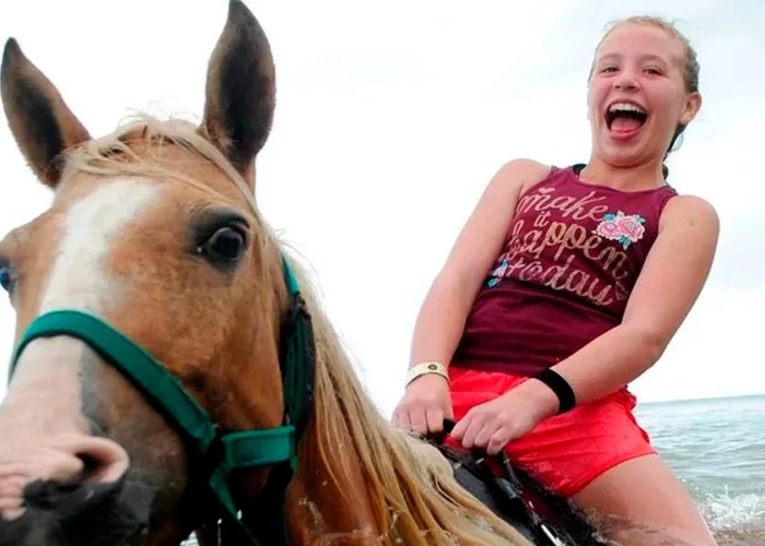Scenic horse riding experience on the beach, with riders trotting along the shoreline, the gentle waves lapping at their feet, and the sun setting in the background, creating a tranquil and picturesque coastal adventure.