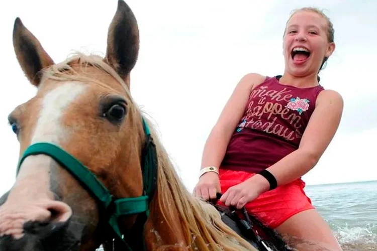 Scenic horse riding experience on the beach, with riders trotting along the shoreline, the gentle waves lapping at their feet, and the sun setting in the background, creating a tranquil and picturesque coastal adventure.