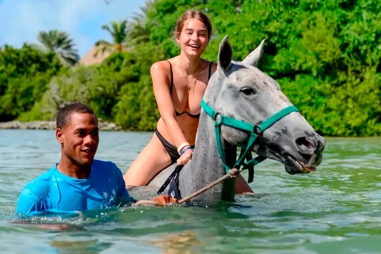 Scenic horse riding experience on the beach, with riders trotting along the shoreline, the gentle waves lapping at their feet, and the sun setting in the background, creating a tranquil and picturesque coastal adventure.