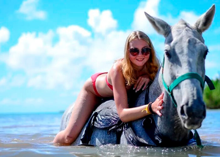 Scenic horse-riding experience on the beach, with riders trotting along the shoreline, the gentle waves lapping at their feet, and the sun setting in the background, creating a tranquil and picturesque coastal adventure.