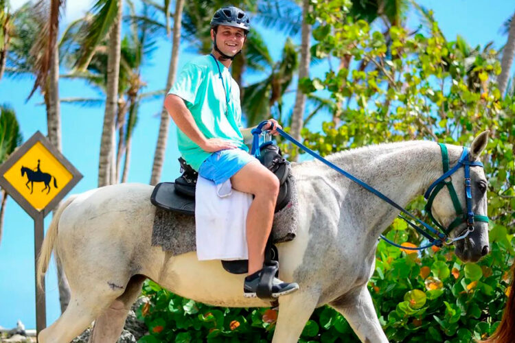 Scenic horse riding experience on the beach, with riders trotting along the shoreline, the gentle waves lapping at their feet, and the sun setting in the background, creating a tranquil and picturesque coastal adventure.