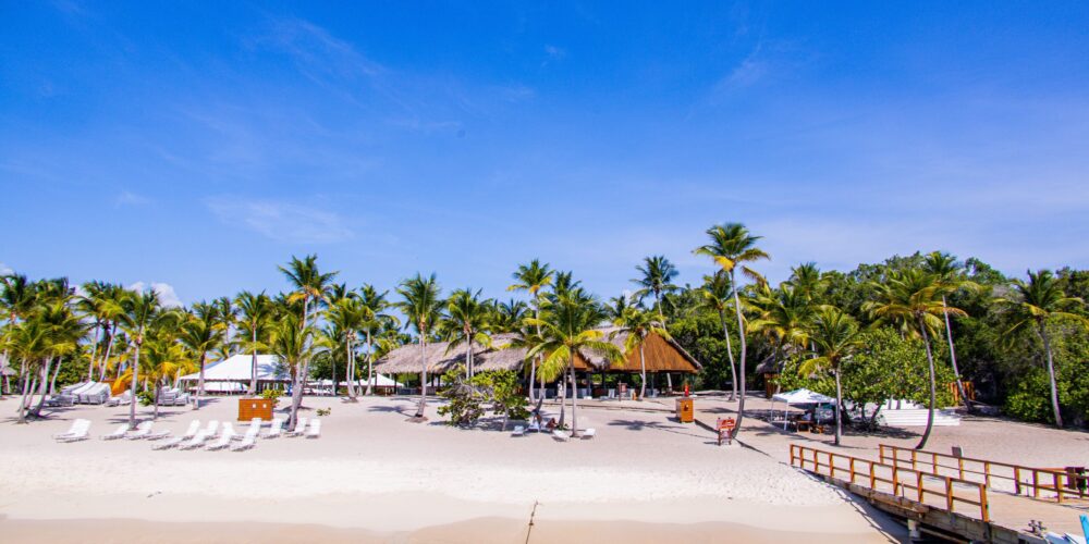 Sunbathers and beachgoers enjoying the pristine white sands and crystal-clear waters of Catalina Beach, relaxing under umbrellas, swimming, and engaging in beach activities in a picturesque tropical setting.