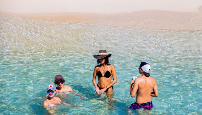 Sunbathers and beachgoers enjoying the pristine white sands and crystal-clear waters of Catalina Beach, relaxing under umbrellas, swimming, and engaging in beach activities in a picturesque tropical setting.