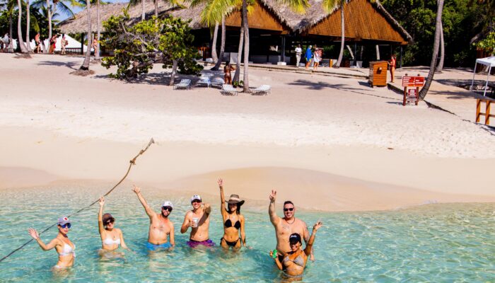 Sunbathers and beachgoers enjoying the pristine white sands and crystal-clear waters of Catalina Beach, relaxing under umbrellas, swimming, and engaging in beach activities in a picturesque tropical setting.