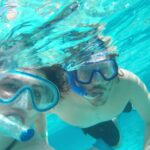 Participants snorkeling in clear, turquoise waters, wearing masks and snorkels to explore vibrant coral reefs and colorful marine life, enjoying an underwater adventure in a tropical setting.